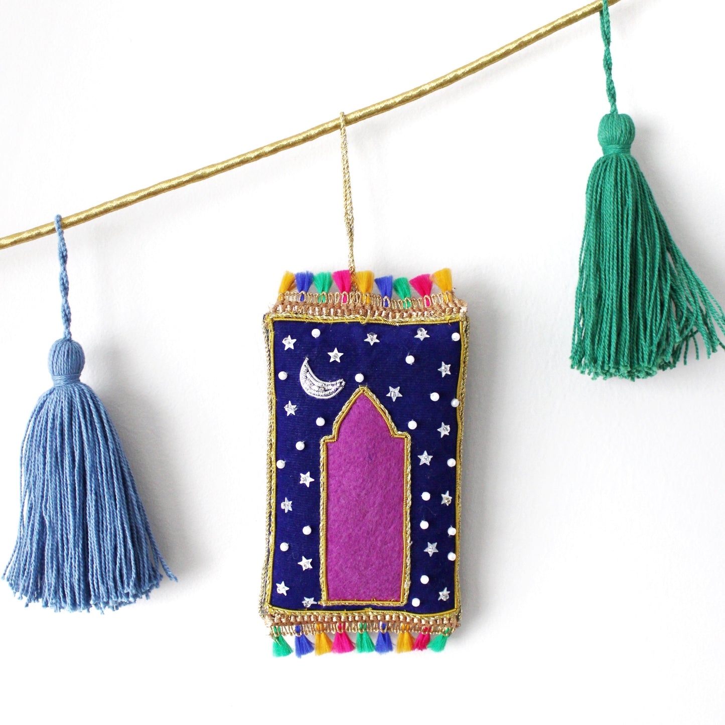 A collection of various handmade ornaments including representations of religious and cultural symbols such as the Kabaah, a mosque, a Quran, and other significant items for Muslims, along with tassels and a gold display cord.