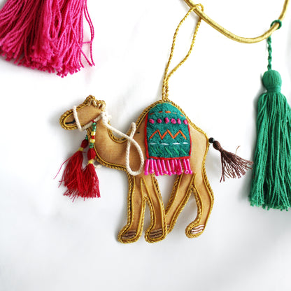 A collection of various handmade ornaments including representations of religious and cultural symbols such as the Kabaah, a mosque, a Quran, and other significant items for Muslims, along with tassels and a gold display cord.