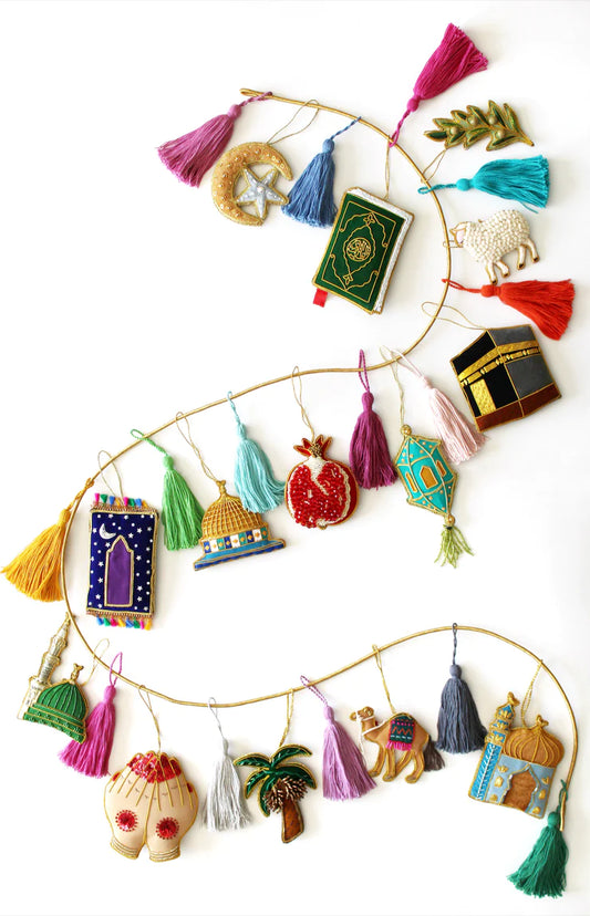 A collection of various handmade ornaments including representations of religious and cultural symbols such as the Kabaah, a mosque, a Quran, and other significant items for Muslims, along with tassels and a gold display cord.