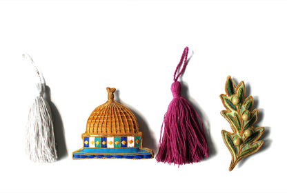 A collection of various handmade ornaments including representations of religious and cultural symbols such as the Kabaah, a mosque, a Quran, and other significant items for Muslims, along with tassels and a gold display cord.