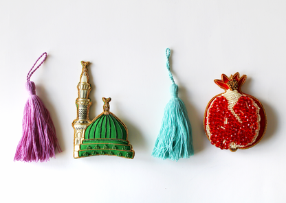 A collection of various handmade ornaments including representations of religious and cultural symbols such as the Kabaah, a mosque, a Quran, and other significant items for Muslims, along with tassels and a gold display cord.